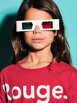 Portrait of happy preteen girl in white plastic stereoscopic glasses with red and blue lens smiling at camera while watching 3d graphic film with pleasure against turquoise background in modern studio