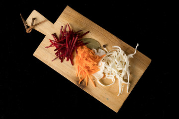 Top view of a wooden chopping Board with cabbage, beets and carrots on a black background diagonally