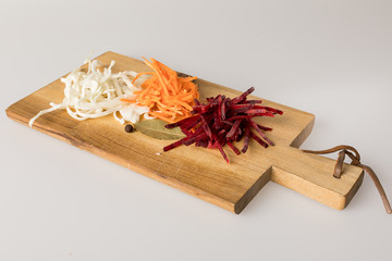 Wooden cutting Board with cabbage, beets and carrots on a white background.