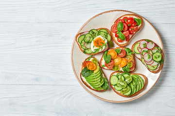 Italian vegan bruschetta on wooden background. Open sandwiches with avocado, cherry tomato, cucumber, radish. Various sandwich with spinach isolated on white, top view. Flat lay