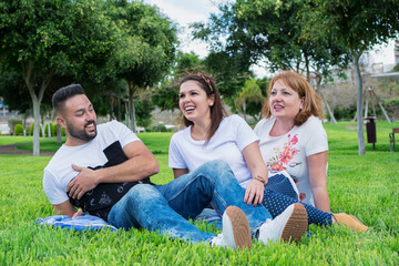 Two brothers boy and girl with their mother happy and laughing sitting on the green grass of the park.