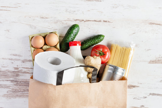 Paper shopping bag with various food top view on white wooden background. Food donation, safe delivery service concept.