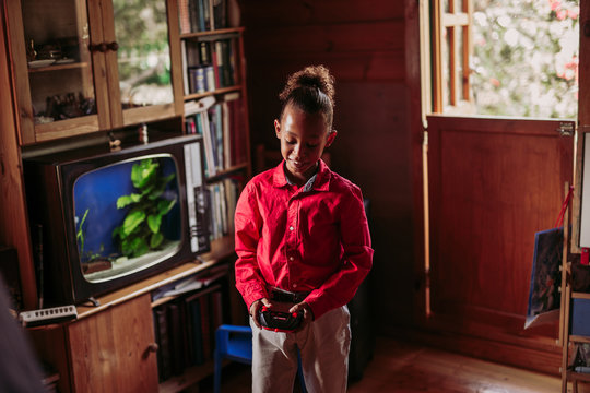 Positive black teen girl in casual clothes with joystick controller in hands playing in room with wooden interior and old fashioned tv