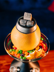 Top view close up of orange hookah bowl with skittles candies around, close up of tropical orange shisha