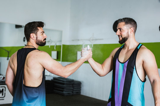 Side view of muscular competitive male bodybuilders with powdered with talcum palms greeting  each other while standing in modern gym