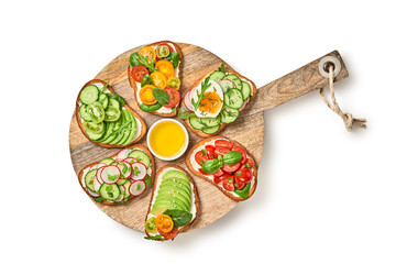 Open sandwiches with avocado, cherry tomato, cucumber, radish. Italian vegan bruschetta on wooden board. Various sandwich with spinach isolated on white, top view. Flat lay