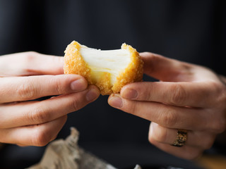 Crop unrecognizable female hands holding delicious mozzarella cheese ball while sitting at table in cafe