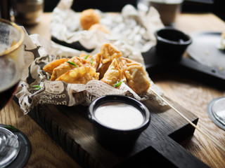 From above top view of delicious deep fried dumplings garnished with green herbs placed on paper served with white sauce on wooden table