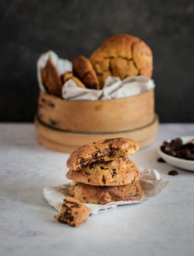 Stack of yummy chocolate chip cookies with bitten piece placed on table near wooden bowl with fresh homemade pastry