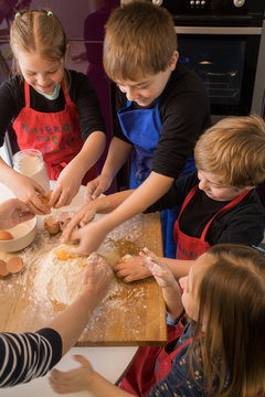 Children preparing dough while standing together at kitchen table with flour