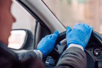 A man holds the steering wheel of a car in protective medical gloves. Hands close-up. Safe drive in a taxi during pandemic coronavirus. Protect driver and passengers from bacteria and virus infection.