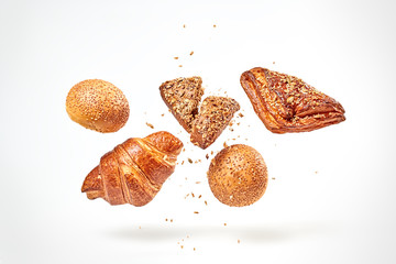 Croissant bun brioche cake flying in air. Fresh baked cookie with sesame, sunflower seed falling on...