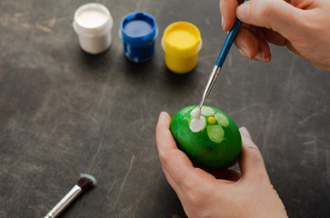 Woman painting with watercolors on egg to prepare Easter eggs.