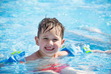 Fototapeta na wymiar Toddler in a children's pool in arm ruffles smiling happy