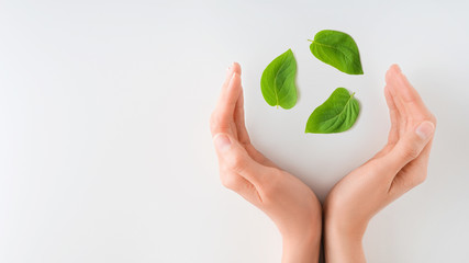 Ecology, protection of natural environment, recycling concept. Woman hands holding recycle symbol made of green leaves, over white background.