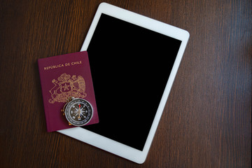 One Red Chilean passport with a white tablet and a compass on a wooden desk