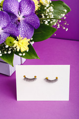 False eyelashes and pink flowers composition on purple background. Beauty products, cosmetics for eyes make up, eyelash extensions, beauty shop or beauty spa salon concept.