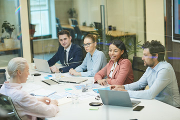 Group of business people sitting behind the glass wall and talking to each other during meeting