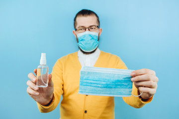 A man in a medical mask with a sanitizer in his hands on a blue background. An emotional guy shows...