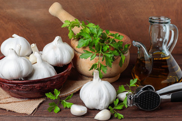 still life with mortar with parsley, bowl with garlic heads, oil pourer and  garlic masher on a table and wodd background