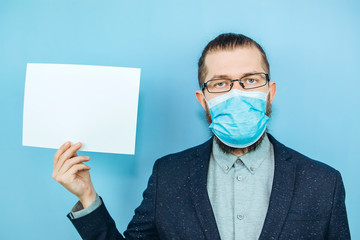 A man in a suit, glasses and a medical mask holds a piece of paper, on a blue background. Place for text. Businessman holds a tablet in his hands. The problem of business due to coronavirus. COVID-19