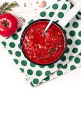 Homemade tomato sauce with herbs and garlic in a white pan on a white wooden table, top view, copy space. Bowl with homemade ketchup, tomatoes and herbs on a white background, free space for text