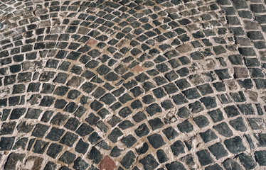 The old dark gray paving stones laid out in a semicircle. The texture of the old dark stone. Road surface. Vintage, grunge.