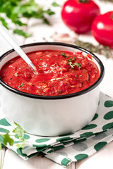 Spicy homemade tomato sauce with herbs and garlic in a white pan on a white wooden table. Pan with homemade ketchup, tomatoes and herbs on a light background.