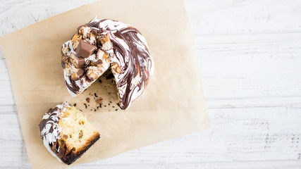 Cake with icing and chocolate glaze on backing paper. Sweet food. White wooden background.