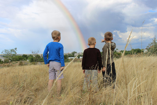 Three boys look at a rainbow in the sky.