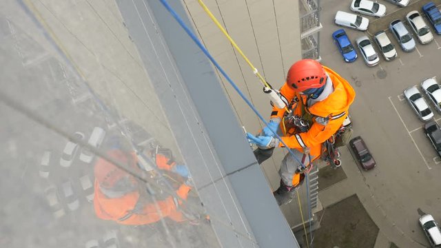 industrial climber hangs on tall building and puts on rubber gloves for working at height before washing windows, fighting the coronavirus pandemic
