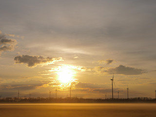Wind turbines generating renewable energy, morning beautiful sunrise light with drifting fog and amazing clouds background.