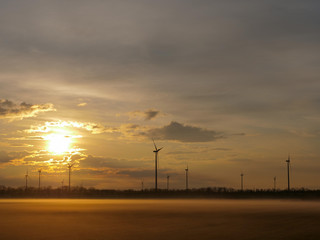Fototapeta na wymiar Wind turbines generating renewable energy, morning beautiful sunrise light with drifting fog and amazing clouds background.