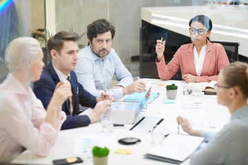 African female businesswoman talking to her colleagues while they sitting at the table during business meeting at office