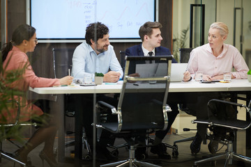 Mature businesswoman talking to her colleagues at the table and they listening to her during business meeting at office
