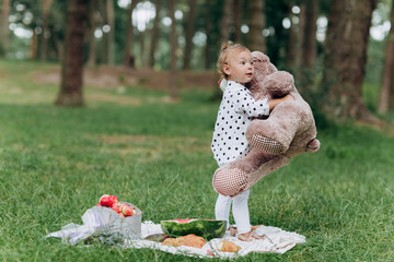 Adorable little toddler girl with a big teddy bear having fun in the summer park on sunny day. concept of summer holiday picnic. selective focus