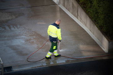 Janitor washes the yard with water from a hose.