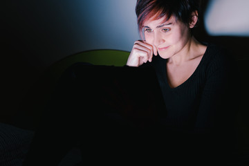 Social distance concept during coronavirus isolation. European woman watching tv news with tablet device at night. People addicted to new technologies concept. Stay home lifestyle.