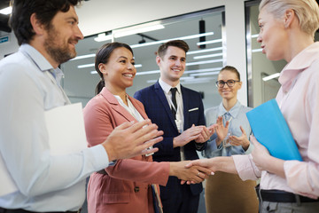 Two businesswomen shaking hands after successful agreement with other business people who standing...