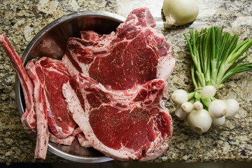 Some fresh sirloin steaks in a bowl and some green onions on a table