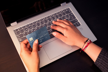Female hands holding a credit card for making payment transaction with laptop on wood table. Online...