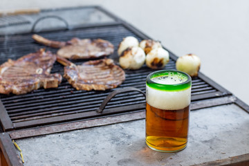 Fresh beer and some pieces of meat on a grill