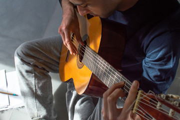 Top view of a young man playing guitar and composing music at home. Casual man sitting on the floor...