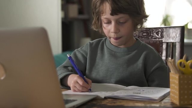 young student boy e-learning at home during quarantine. Spbd online distant school learning. concentrated schoolboy stays home and draws writes in book using laptop. concept technology