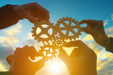 Four hands of businessmen collect gear from the gears of the details of puzzles. against the background of sunlight. The concept of a business idea. Teamwork. strategy. Collaboration, partnership