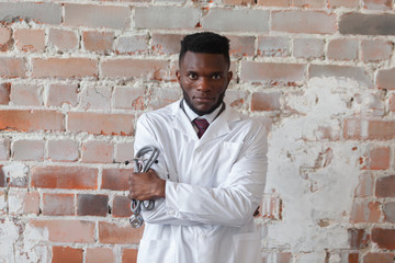 Obraz premium Black man doctor holding stethoscope is ready to fight against the COVID, COVID-19, coronavirus, pandemic, epidemic, virus against a red brick wall. Concept of humanitarian assistance to African