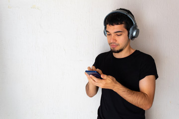 Fototapeta premium Young Hispanic man with black clothes listening to music with headphones on his head on a white background