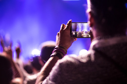 Manos sujetando tel&eacute;fono m&oacute;vil grabando un festival de m&uacute;sica
