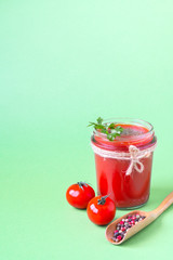 Tomato juice with a leaf of parsley in a glass jar, fresh tomatoes and a wooden spoon with pepper. Light green background, copy space.