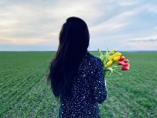 a girl in summer dress with bouquet of tulips in green field